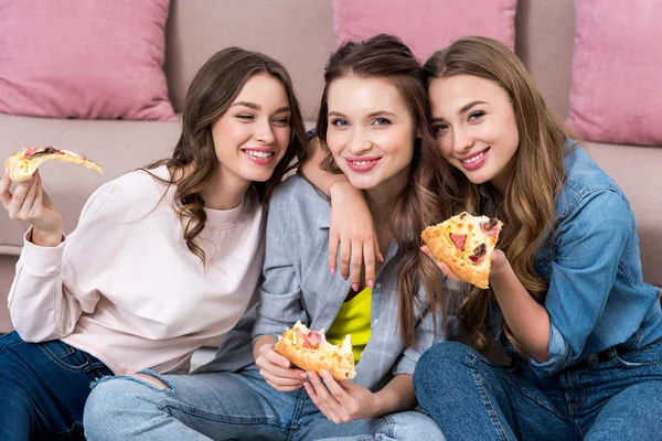 Hermosas mujeres jóvenes comiendo pizza y sonriendo a la cámara - foto de stock