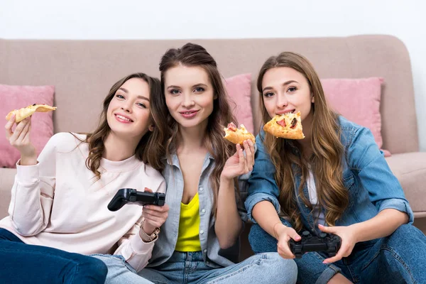 Beautiful smiling girlfriends eating pizza and playing with joysticks — Stock Photo