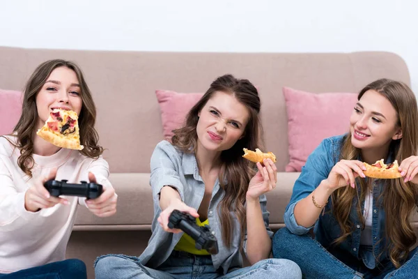 Belles jeunes femmes mangeant de la pizza et jouant avec des joysticks — Photo de stock
