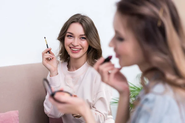 Enfoque selectivo de las mujeres jóvenes sonrientes aplicando maquillaje juntos en casa - foto de stock