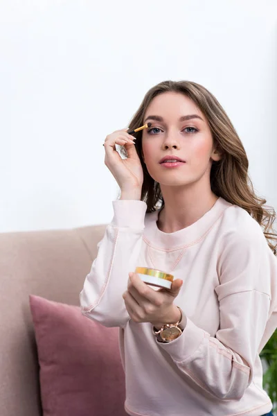 Beautiful young woman applying makeup and looking at camera — Stock Photo