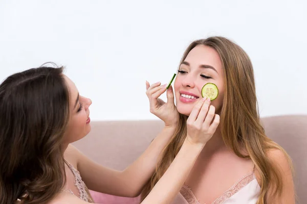 Chica atractiva sosteniendo rodajas de pepino cerca de la cara de la novia sonriente - foto de stock