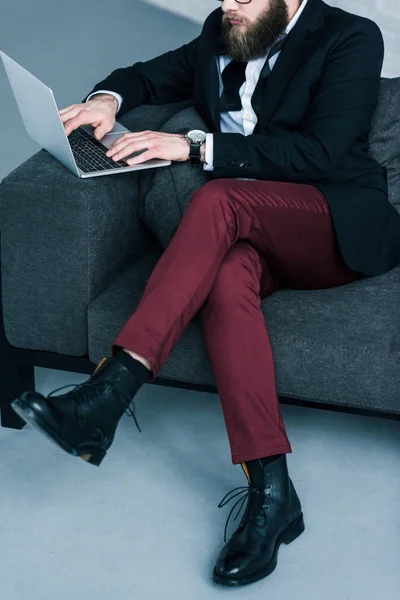 Visão parcial do homem de negócios elegante sentado no sofá e usando laptop — Fotografia de Stock