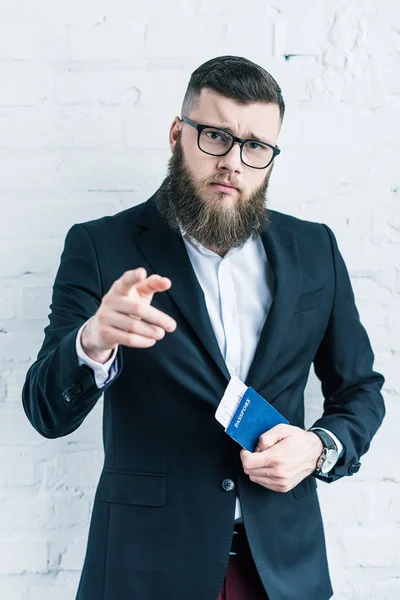 Portrait of businessman with passport and ticket in hand pointing at camera — Stock Photo