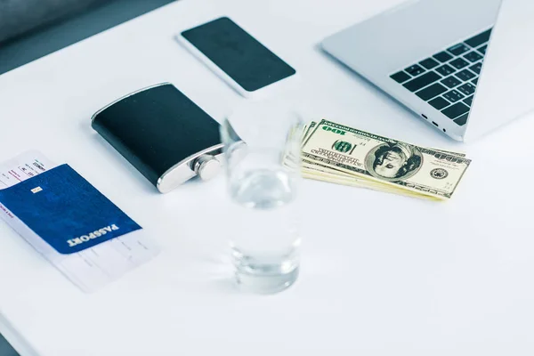 Vue rapprochée du verre d'eau, du flacon, du passeport avec billet, de l'argent, du smartphone et de l'ordinateur portable sur la table — Photo de stock