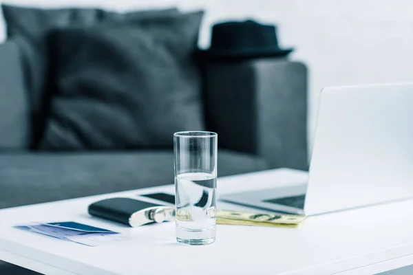 Selective focus of glass of water, flask, passport with ticket, money, smartphone and laptop on tabletop — Stock Photo