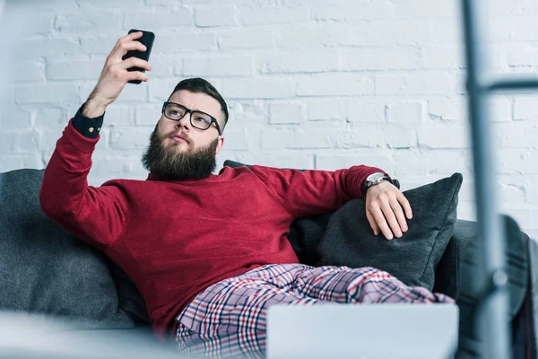 Porträt eines Geschäftsmannes, der sich auf dem Sofa ausruht und sein Smartphone benutzt — Stockfoto