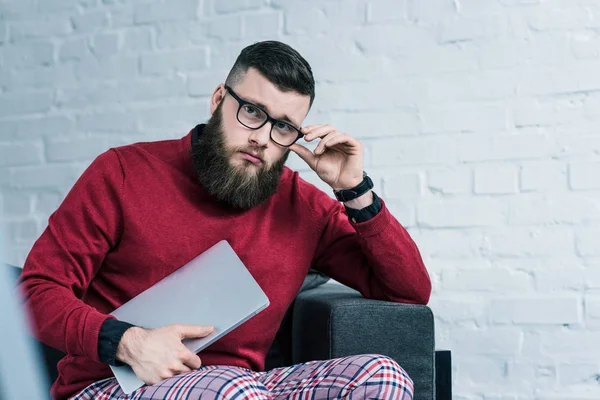 Portrait of stylish businessman in eyeglasses with laptop sitting on sofa — Stock Photo