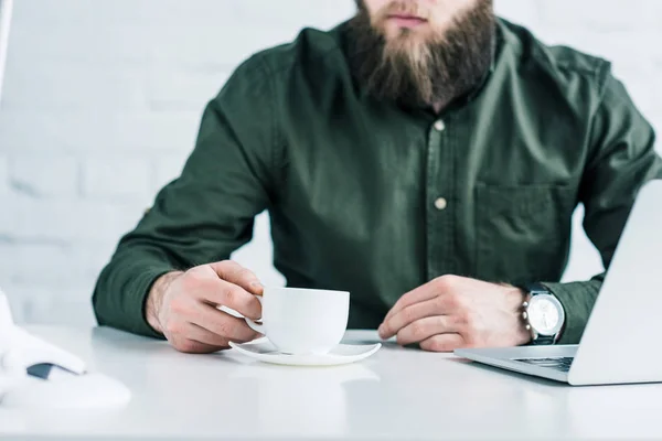 Recortado tiro de hombre de negocios con taza de café en el lugar de trabajo - foto de stock