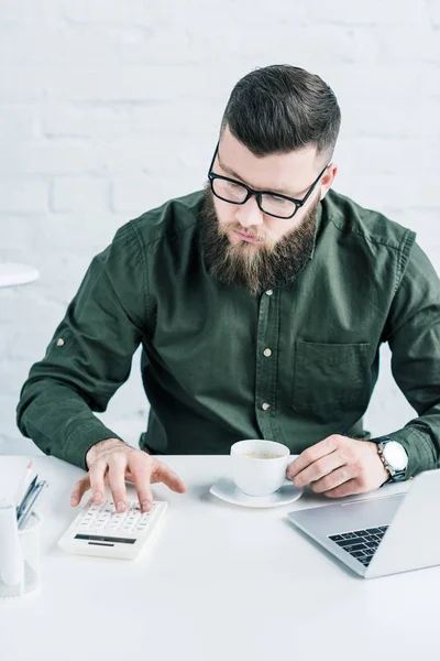 Porträt eines fokussierten Geschäftsmannes, der bei einer Tasse Kaffee am Arbeitsplatz Berechnungen anstellt — Stockfoto