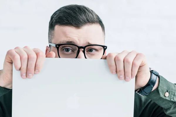 Obscured view of businessman in eyeglasses covering face with laptop — Stock Photo