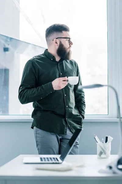 Selective focus of pensive businessman with cup of coffee looking out window — Stock Photo