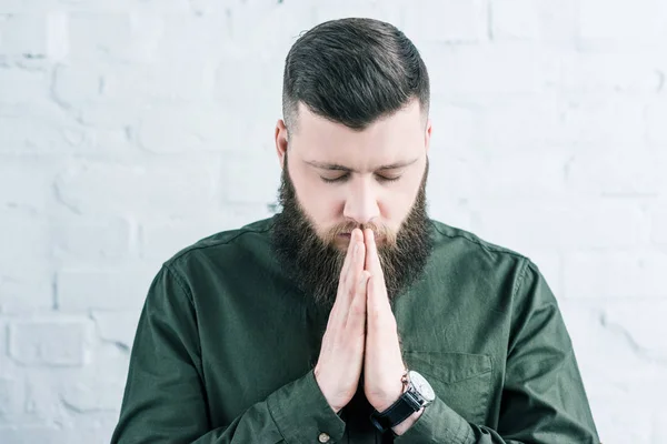 Portrait of stylish bearded man praying against white brick wall — Stock Photo