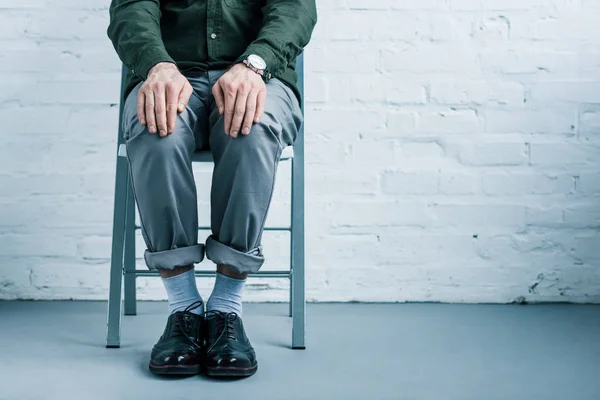 Vue partielle de l'homme d'affaires assis sur une chaise contre un mur de briques blanches — Photo de stock