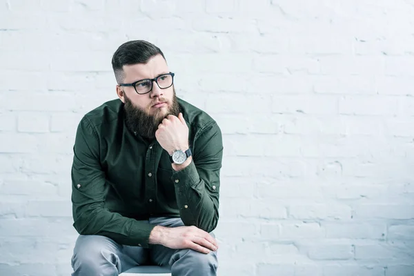 Porträt eines nachdenklichen Geschäftsmannes, der auf einem Stuhl vor einer weißen Backsteinwand sitzt — Stockfoto