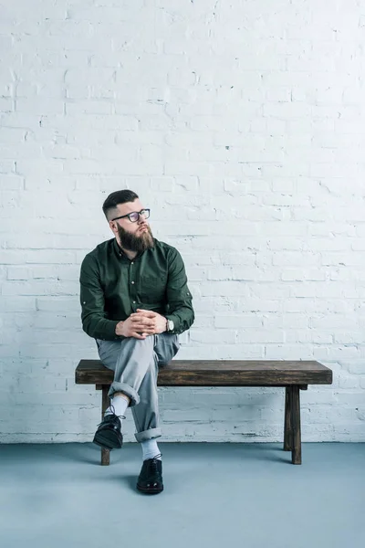 Nachdenklicher Geschäftsmann sitzt auf Holzbank vor weißer Backsteinwand — Stockfoto