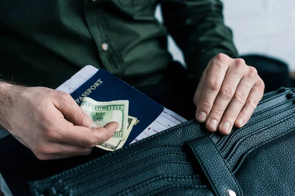 Recortado tiro de hombre de negocios poner pasaporte, billete y dinero en la maleta - foto de stock