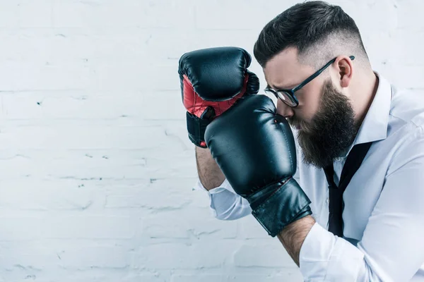 Seitenansicht des Geschäftsmannes in Boxhandschuhen, der sein Gesicht gegen eine weiße Ziegelwand abdeckt — Stockfoto