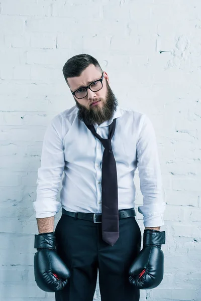 Портрет печального бизнесмена в боксёрских перчатках на стене из белого кирпича — стоковое фото