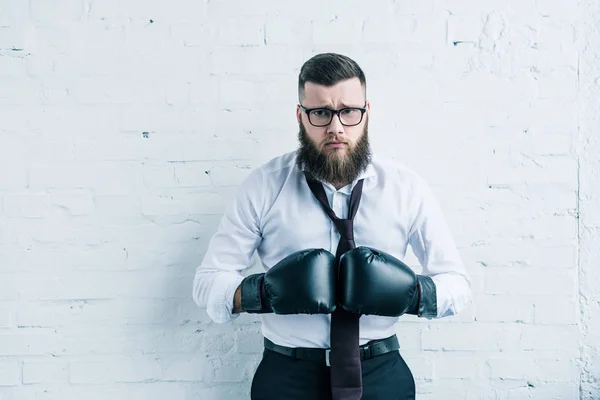 Retrato de empresario molesto en guantes de boxeo mirando hacia otro lado contra la pared de ladrillo blanco - foto de stock