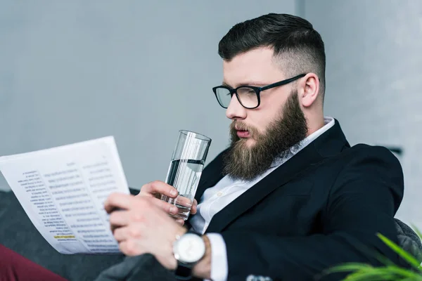Side view of focused businessman with glass of water in hand reading newspaper — Stock Photo