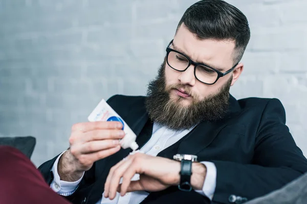 Портрет бородатого бізнесмена в окулярах наносячи крем на руку — стокове фото