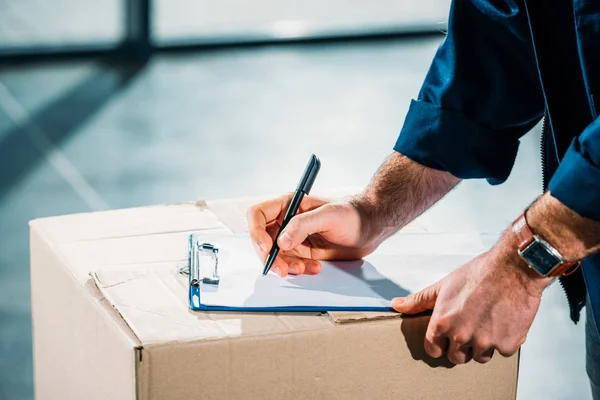 Courier filling cargo declaration on cardboard package — Stock Photo