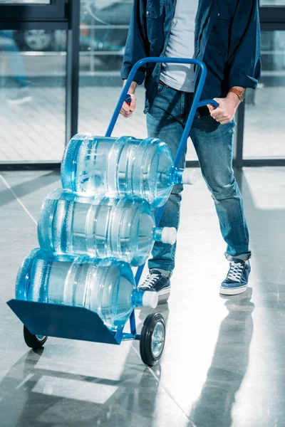 Consegna uomo spingendo carrello con bottiglie d'acqua — Foto stock