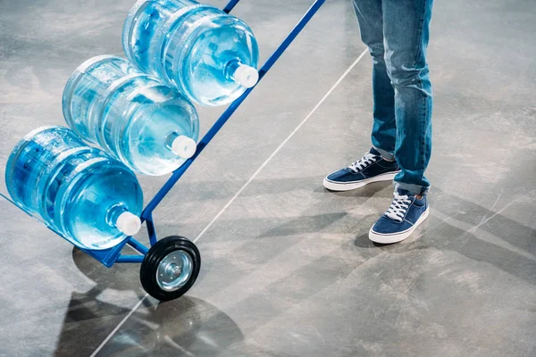 Vista de cerca del hombre cargador de pie junto al carro con botellas de agua - foto de stock