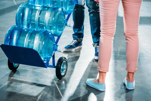 Cropped view of woman standing next to courier delivering water — Stock Photo