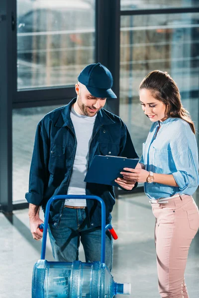 Woman and courier delivering water looking at cargo declaration — Stock Photo