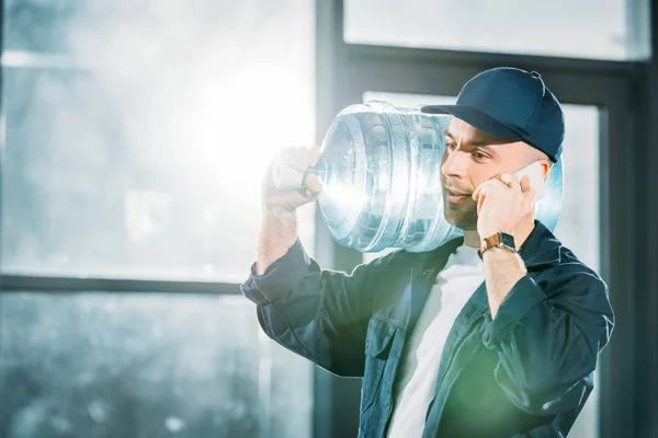 Entrega cara carregando garrafa de água e falando no telefone — Fotografia de Stock