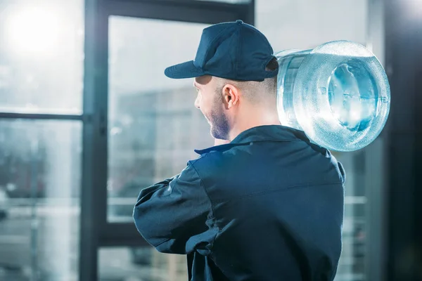 Visão traseira do carregador carregando garrafa de água no ombro — Fotografia de Stock