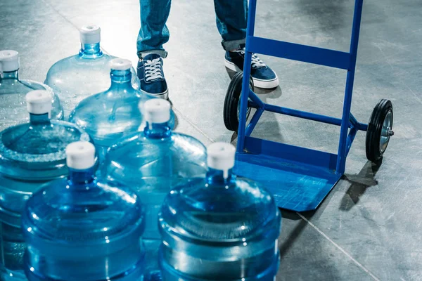 Cargador hombre con carro de entrega de pie junto a botellas de agua - foto de stock