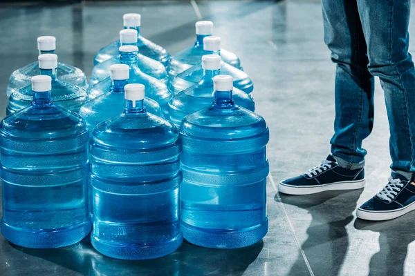 Courier standing by large bottles with drinking water — Stock Photo