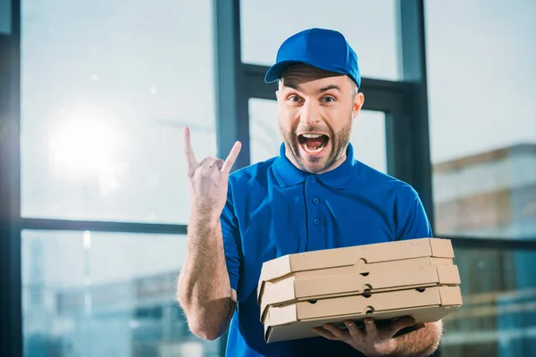 Emocionado mensajero con pizzas en cajas que muestran señal de roca - foto de stock