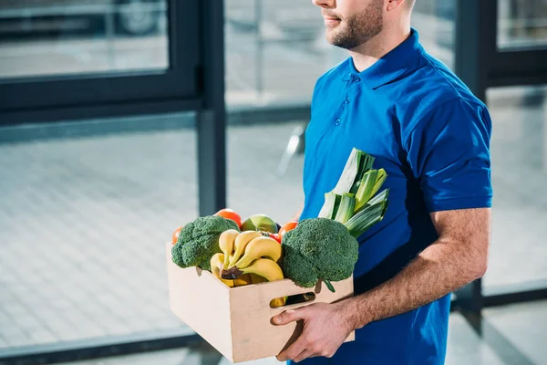 Курьер держит коробку со свежими фруктами и овощами — стоковое фото