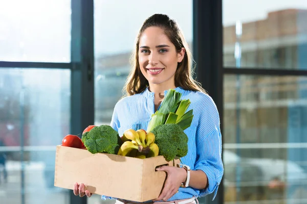 Mujer sonriente sosteniendo caja con comestibles - foto de stock