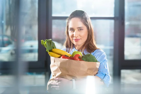 Smiling woman holding paper bag with fresh fruits and vegetables — Stock Photo