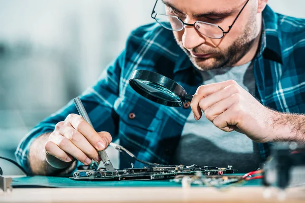 Engineer fixing circuit board looking through magnifying glass — Stock Photo