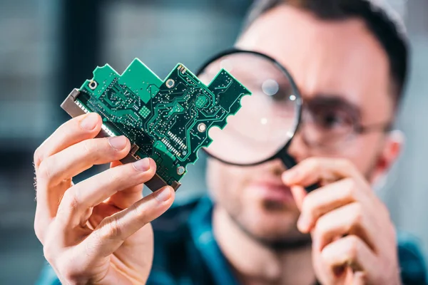 Close-up view of man looking at circuit board through magnifying glass — Stock Photo