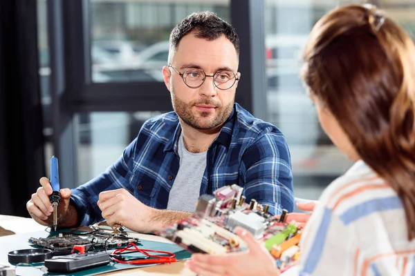 Mujer sosteniendo placa de circuito mientras ingeniero soldadura de piezas de computadora - foto de stock