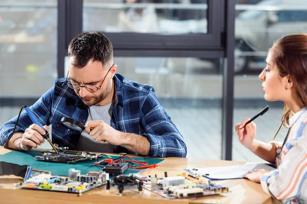 Mujer llenando lista de verificación mientras ingeniero soldadura de piezas de computadora - foto de stock