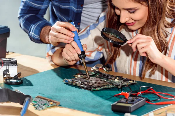 Man helping woman soldering elements of circuit board — Stock Photo