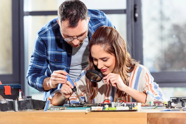 Female and male engineers soldering circuit board — Stock Photo