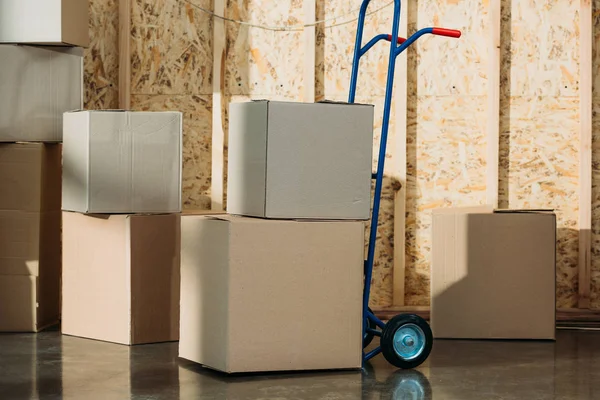 Cardboard packages and delivery cart in warehouse room — Stock Photo