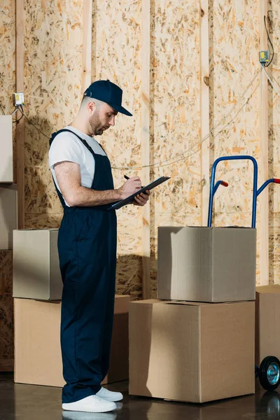 Loader man filling cargo declaration by delivery cart — Stock Photo