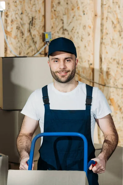 Smiling delivery man holding hand truck — Stock Photo