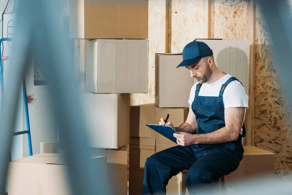 Zusteller füllt Frachtbrief aus, während er an Kisten sitzt — Stockfoto