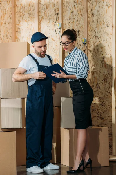 Entrega hombre y mujer de negocios mirando la declaración de carga por pilas de cajas - foto de stock